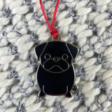 Black pug-shaped pendant on a red string against a textured fabric background
