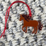 Brown horse-shaped pendant on a red string against a textured white and gray background