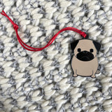 Pug-shaped pendant on a red string against a textured fabric background