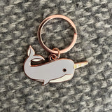 Narwhal-shaped keychain with rose gold accents on a textured gray background