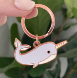 Rose gold narwhal keychain held by a hand with a blurred green leafy background