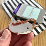 Hand holding a narwhal-shaped keychain with a striped background