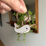 Keychain with a narwhal design held by a hand against a blurred indoor background